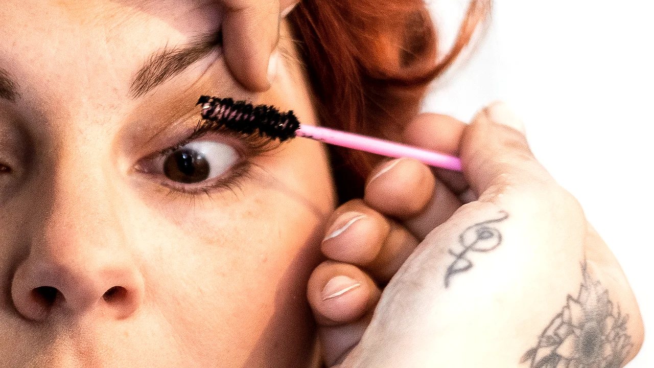 Oog van de bruid in close-up tijdens mascara, getatoeëerde hand van MUA